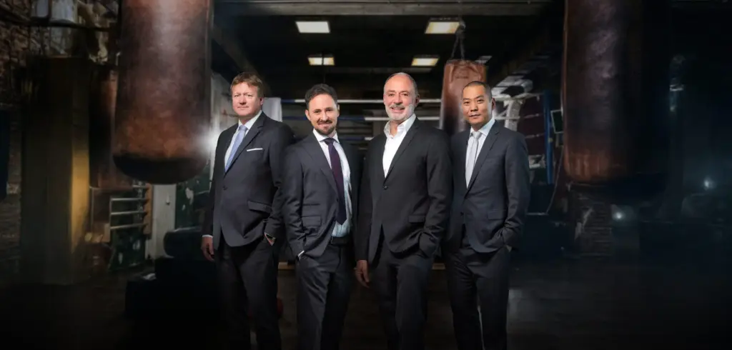 Vier Männer in Anzügen in einer Halle.