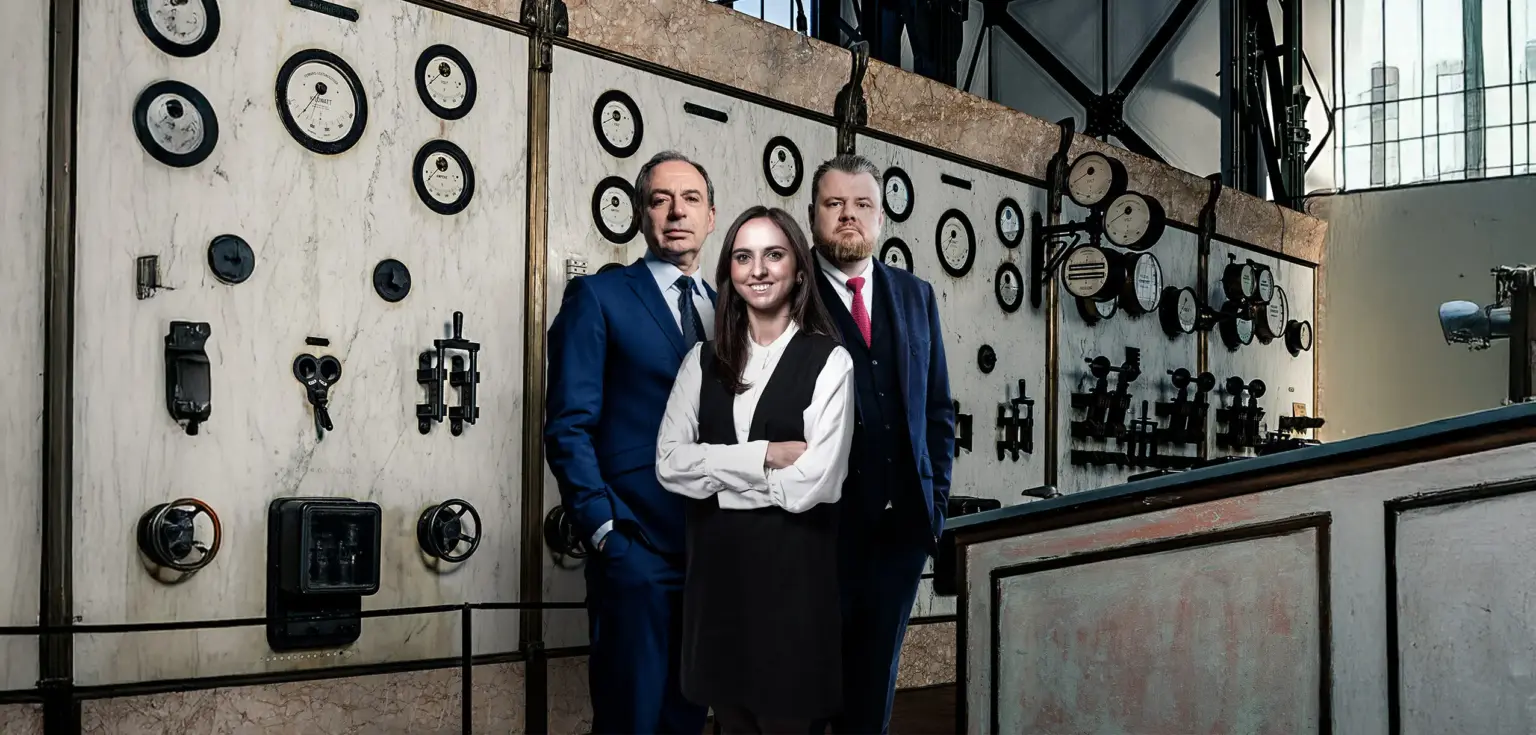 Drei Personen vor vintage Messgeräten in einem Raum.