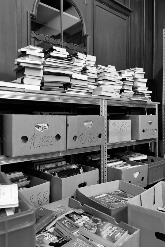 Unsortierte Bücherstapel und Archivboxen in einem Lagerraum