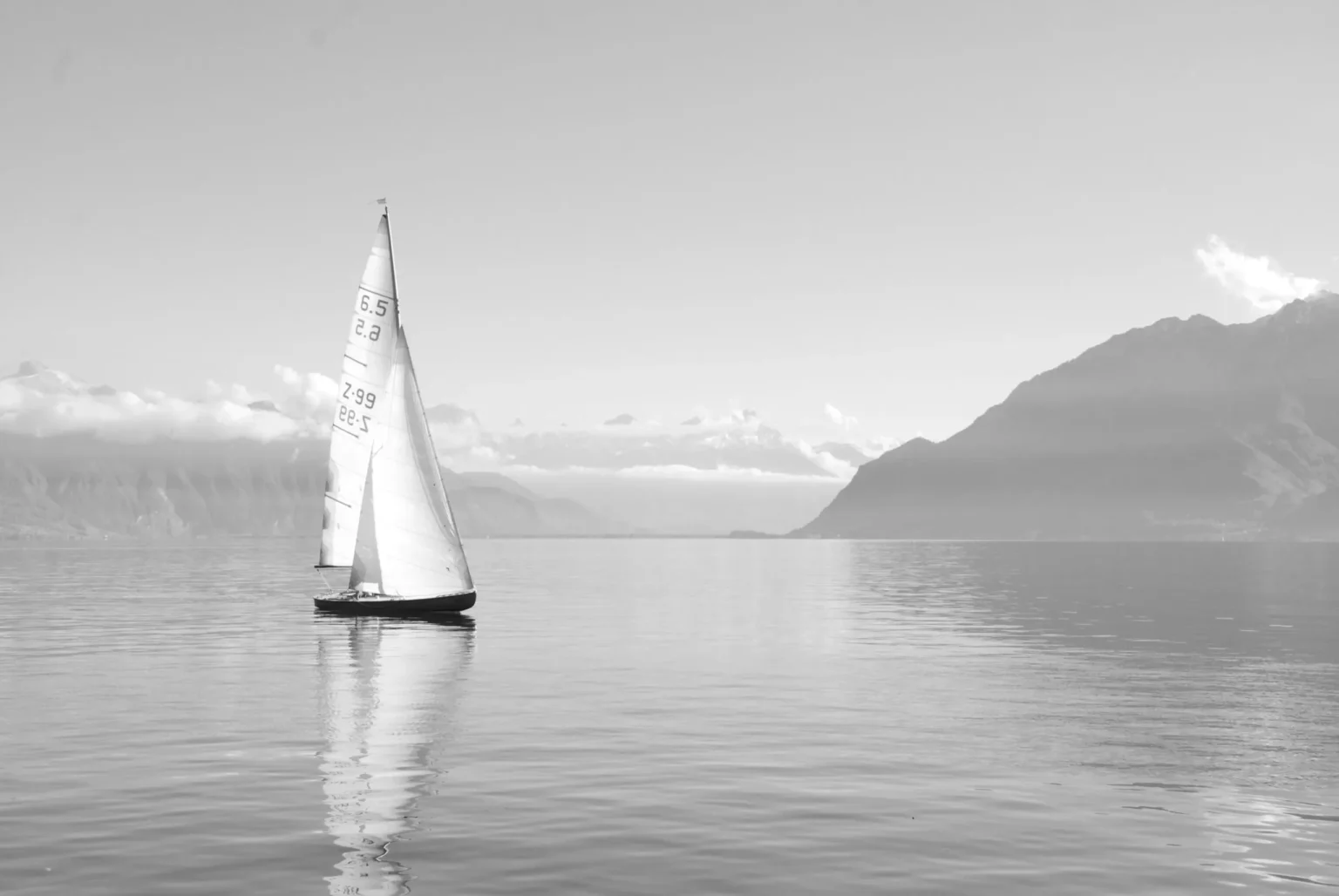 Segelboot auf ruhigem Wasser mit Bergen im Hintergrund