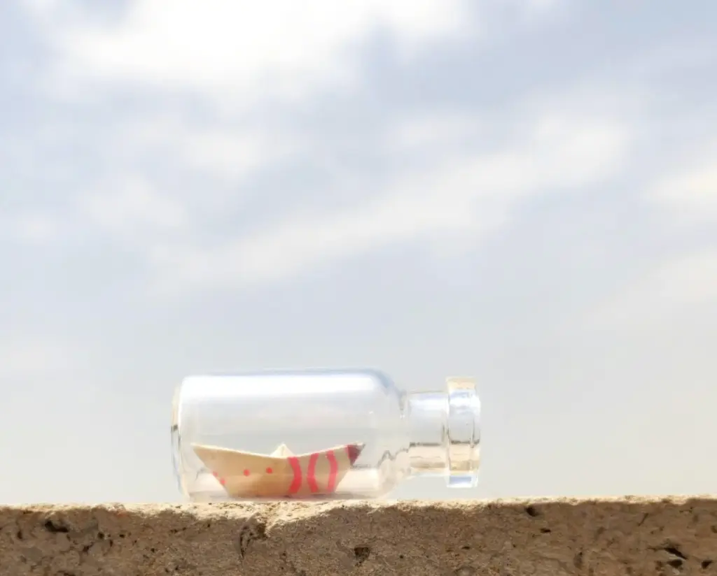 Paper boat inside a glass bottle outdoors.